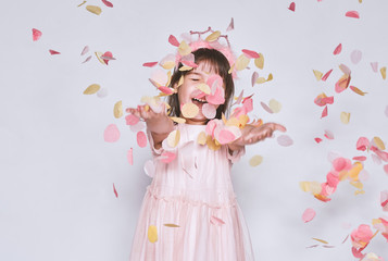 Studio image of happy little girl wearing pink dress with princess crown on head isolated on white background enjoy confetti surprise. Playful smiling girl celebrating her birthday party, having fun