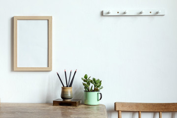 The vintage interior with mock up poster frame, plants, cup with pencils and chair. The vintage concept of space. 