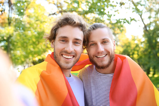 Happy gay couple taking selfie with rainbow LGBT flag in park
