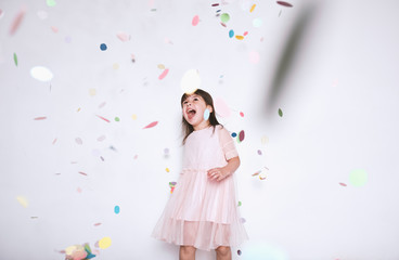 Happy beautiful little girl wearing pink dress with princess crown enjoying colorful confetti...