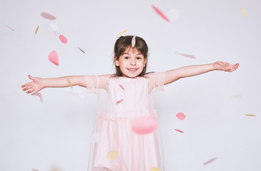 Obraz na płótnie Canvas Image of pretty little girl wearing pink dress in tulle with princess crown on head isolated on white background rise hands enjoy confetti surprise. Cute girl celebrating her birthday party having fun