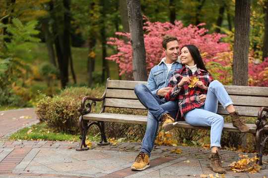 Loving young couple sitting on wooden bench in autumn park