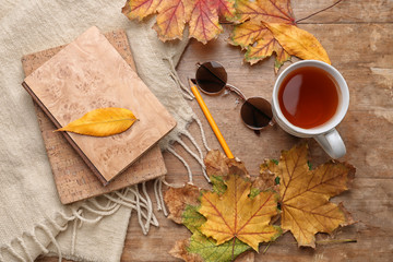 Composition with cup of aromatic tea, warm plaid, books and autumn leaves on wooden background
