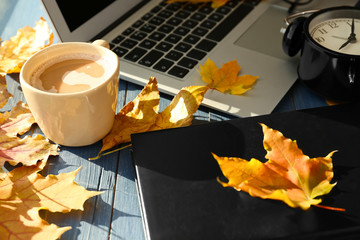Laptop with coffee, book and autumn leaves on wooden table