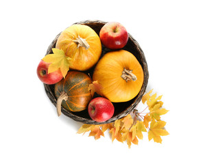 Wicker bowl with fresh pumpkins, apples and autumn leaves on white background