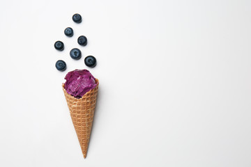 Waffle cone with delicious ice cream and blueberries on white background