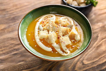 Plate with tasty pumpkin cream soup on wooden table