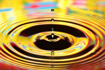Water drops splash in a glass. Yellow colored ripples, reflections on water surface