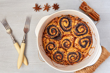 Poppy seed rolls with chocolate topping in the baking dish - traditional Hungarian pastry for Christmas. Cinnamon sweet bread decorated with winter spices on the gray kitchen background. Top view