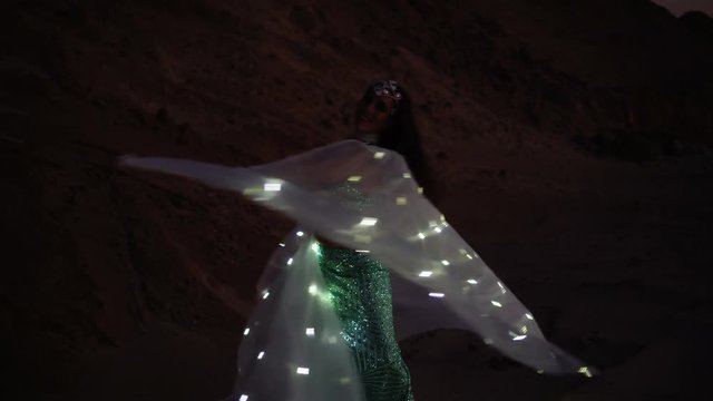 Oriental beauty dancing belly dance with glowing wings. Delightful and alluring grace of movements. Girl dancing in the desert at sunset.