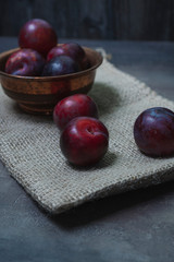 Plums with a bowl on a rural wooden table. Moody and dark style concept. (Prunus domestica)