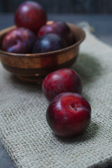 Plums with a bowl on a rural wooden table. Moody and dark style concept. (Prunus domestica)