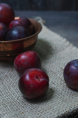 Plums with a bowl on a rural wooden table. Moody and dark style concept. (Prunus domestica)