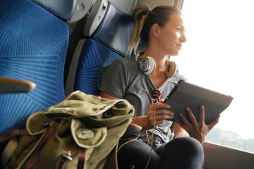 Young woman travelling by train with her tablet and headphones