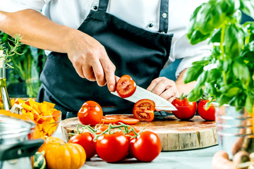 
Chef slicing fresh ripe tomatoes on a board