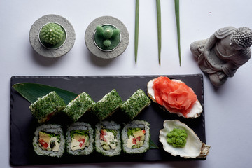 Green sushi set with chuka served on black clay plate with soy sauce and chopsticks, top view. Delicious traditional Japanese food, sushi restaurant concept