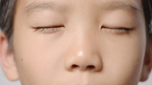 Close up at young Asian boy face and open up his eyes on white background.