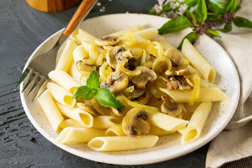 Pasta Penne with mushrooms on a dark stone or concrete table. Vegetarian vegetable mushrooms pasta. Diet menu.