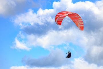 Paraglider with two people (tandem) flying against the blue sky with clouds.
