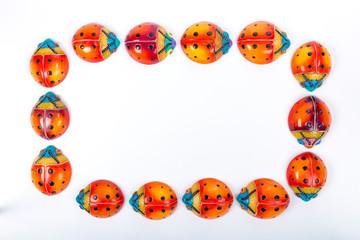 Flat lay with a oval circle formed by a group of fourteen ceramic ladybugs with red, orange, yellow, blue and black colors on a white background. Space for text