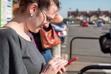 young caucasian woman looking at smartphone in public place outside in british town on sunny day