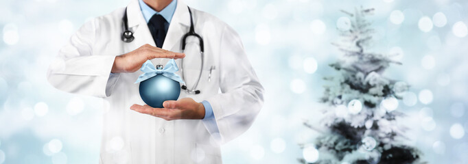 Merry Christmas from doctor,, best wishes concept, hands with xmas ball on blurred light and tree,...