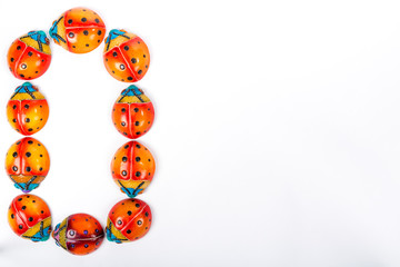 Obraz na płótnie Canvas Flat lay with the letter O or the number 0, formed by a group of ceramic ladybugs with red, orange, yellow, blue and black colors on a white background with space for text