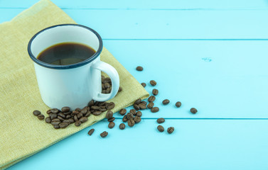 Cup of coffee with coffee beans on blue color wooden background.