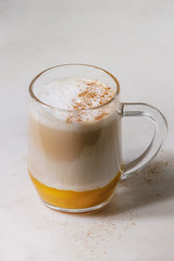 Glass of pumpkin layered spice latte with pumpkin puree, milk foam and cinnamon standing on white marble table. Close up