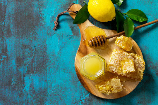 Natural Honey with Lemon. Honey in glass jar and dipper, Sweet Honeycombs on blue stone table. Top view flat lay background. Copy space.