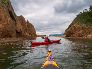 Two sea kayaks sail along the coast on a cloudy day.