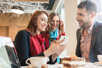 Three young friends using a mobile phone for fun during a coffee break