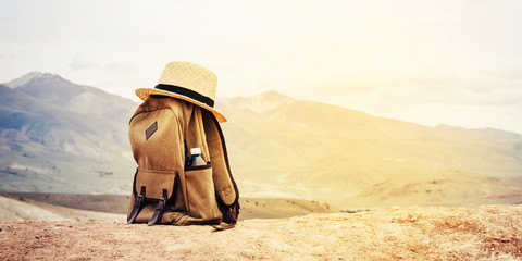 Beige backpack, bottle of water and straw hat on hill in mountains. Active travel concept. Toning...
