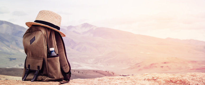 Beige Backpack, Bottle Of Water And Straw Hat On Hill In Mountains. Active Travel Concept. Toning Sunrise