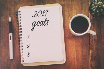 Top view 2019 goals list with notebook, cup of coffee over wooden desk.