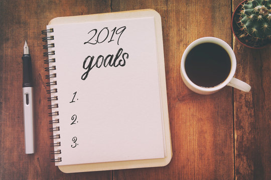 Top view 2019 goals list with notebook, cup of coffee over wooden desk.
