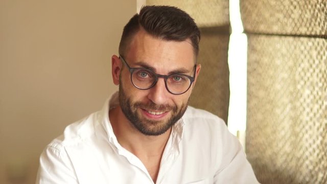 Close portrait of an attractive businessman in glasses and a white shirt. A man looks through his glasses and smiles affably