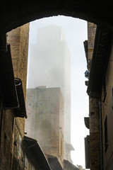 Walking through and under arcades in a narrow alley in San Gimignano, a little perched town with many medieval towers.