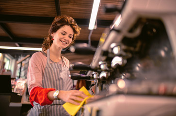 Coffee machine. Pleased female person standing at her workplace while looking downwards