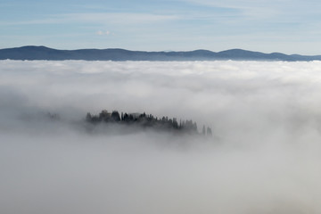 Obraz na płótnie Canvas A view from an high tower in the little town of San Gimignano, tuscany italy. A sea made of fog until the horizon with light blue mountains in the background and a little town emerging from the mist 