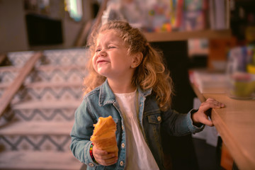 Making face. Cheerful child holding pastry while waiting her mom in cafe