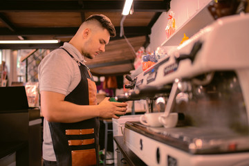 Conscious worker. Serious brunette man bowing head while warming up milk for latte