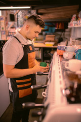 Being serious. Professional coffee maker standing at his workplace while serving his client