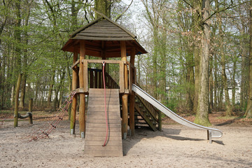 Fototapeta na wymiar playground in forest with wooden hut, climbing contraption and slide