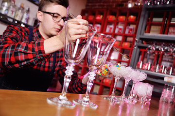 a young bartender prepares a cocktail on the background of the bar. Bartender show