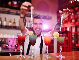 the bartender puts the tubes for cocktails in the prepared alcoholic drinks and smiles against the night club