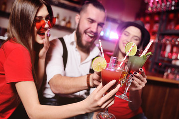 group of friends-young guy and two cute girls having fun at a party holding cocktails