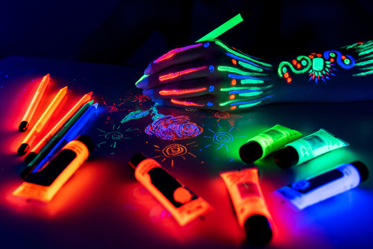 Hand With Fluorescent Ethnic Pattern Holding Neon Pencil. Fluorescent Paint And Pencil Are On The Table. Body Art Concept