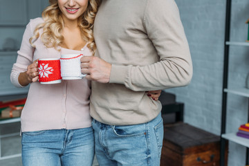 cropped image of couple clinking with cups of tea at home, christmas concept
