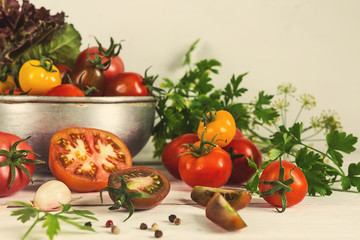 Fresh vegetables tomatoes of different varieties of red yellow in a metal bowl drushlag on a light rustic table, in rustic style tinted horizontal